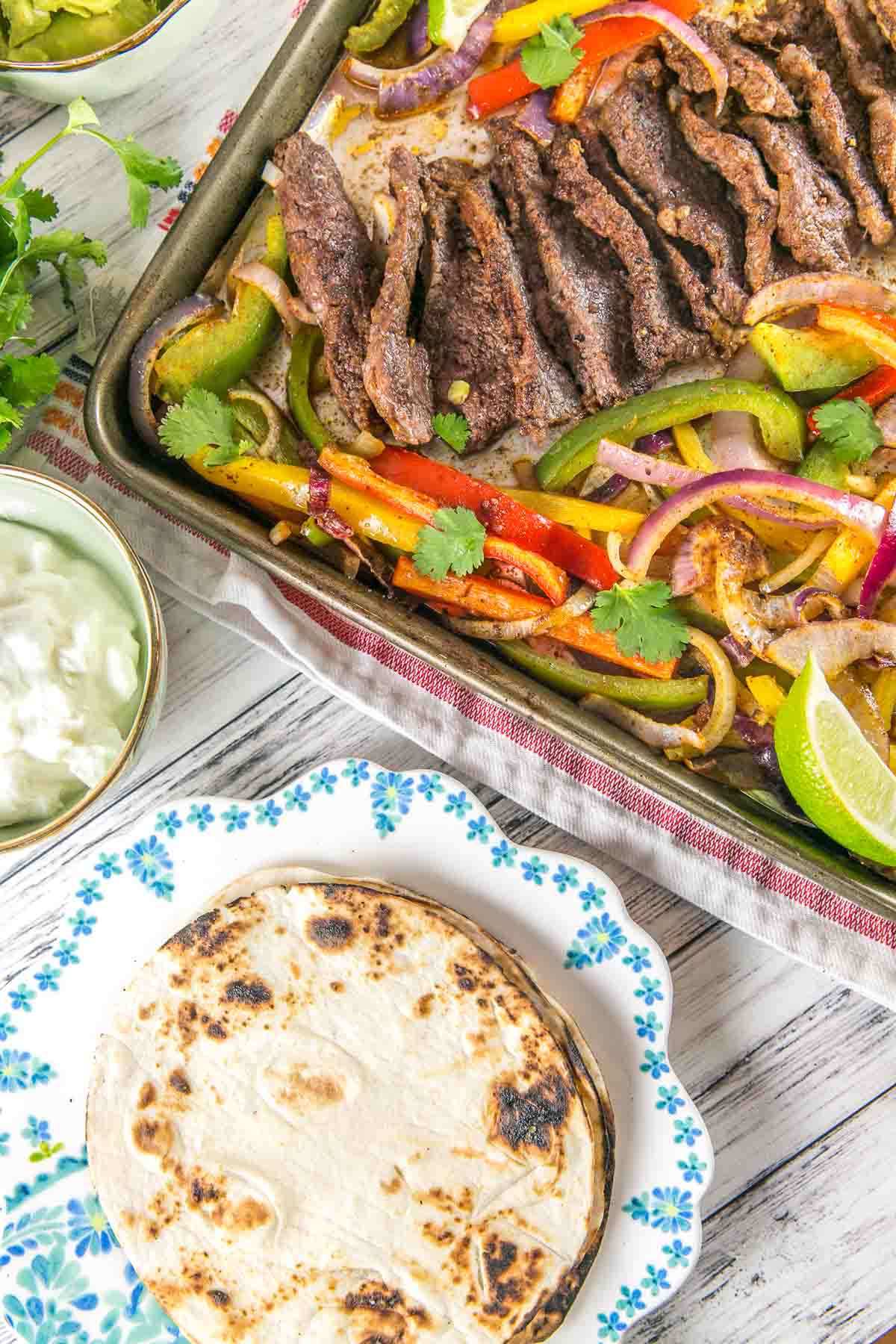 sheet pan steak fajitas next to pan seared flour tortillas