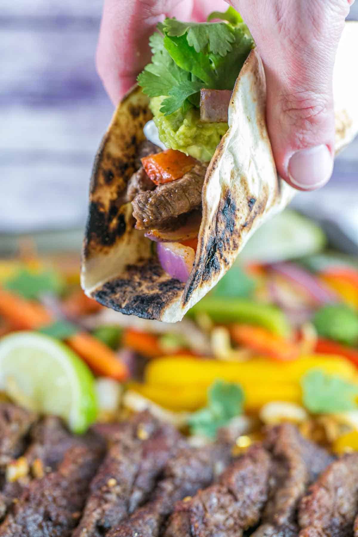 hand picking up a tortilla filled with steak and peppers