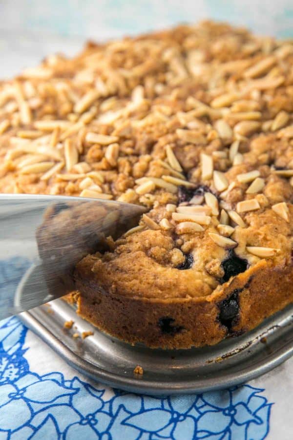 one slice being cut out of a large blueberry almond coffee cake