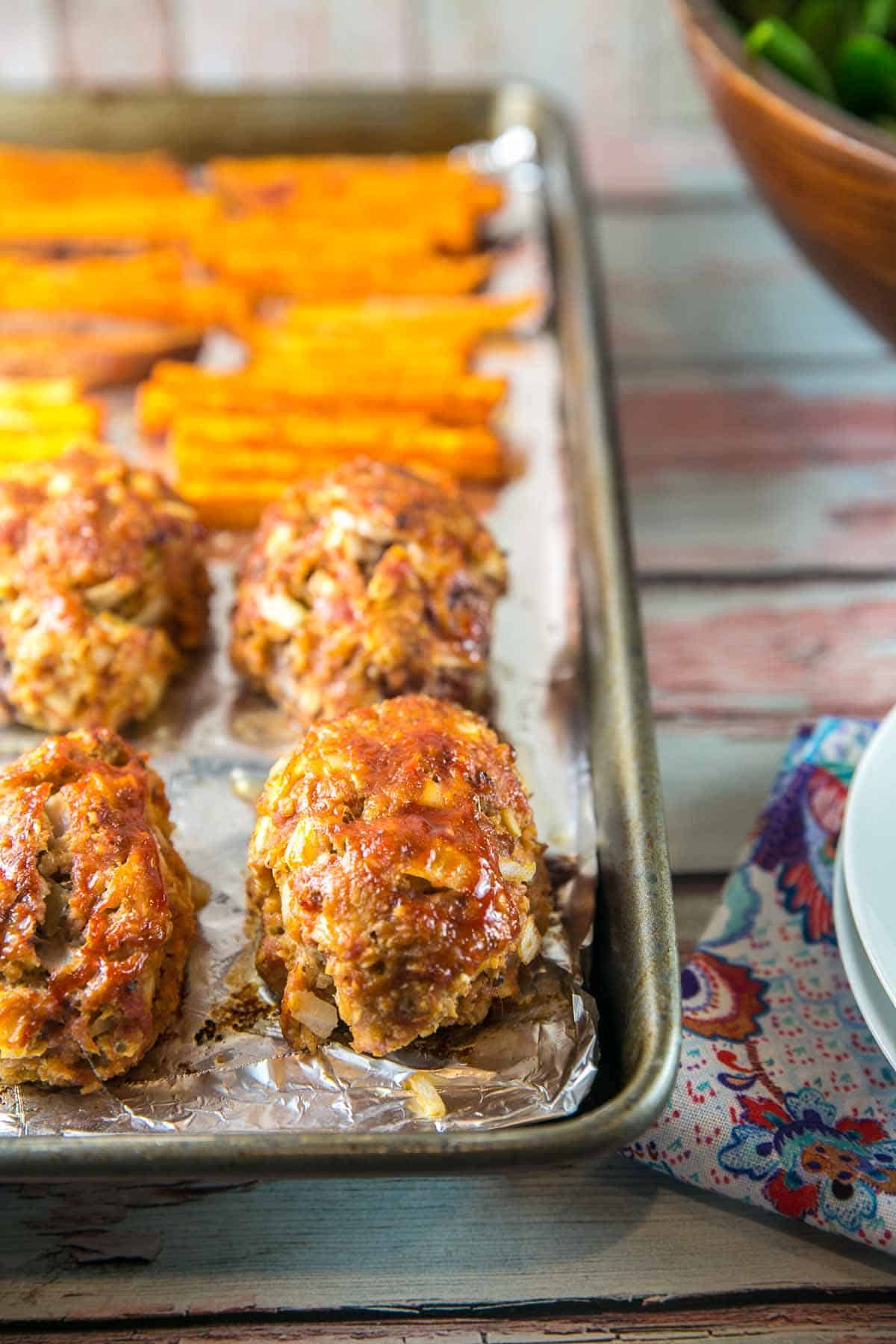 side view of individual sized mini meatloaves on a foil-lined sheet pan