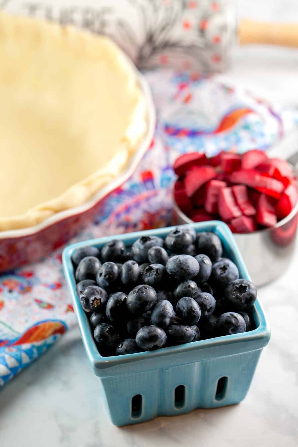 fresh rhubarb and blueberries in pint containers next to an unbaked pie crust