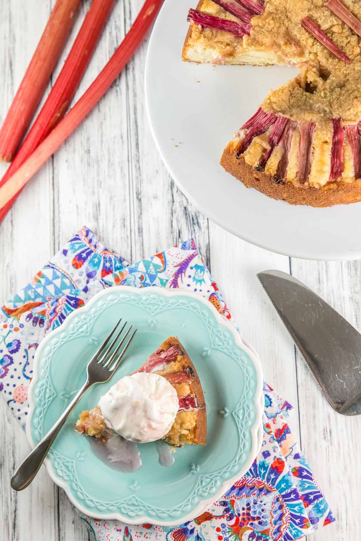 slice of almond rhubarb cake on a blue dessert plate with a big scoop of ice cream