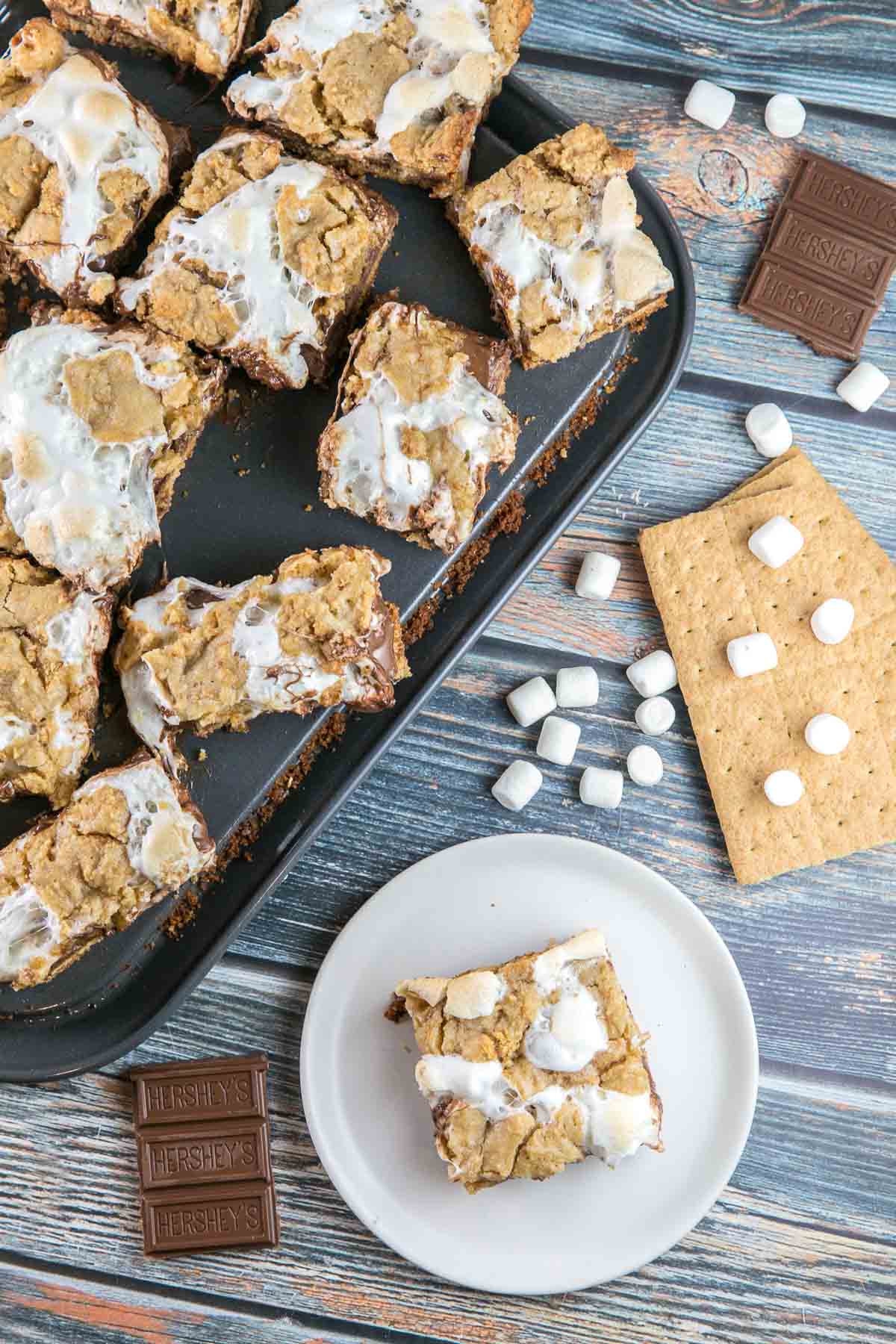 sliced bars on a baking sheet with marshmallows, graham crackers, and chocolate bars in the background
