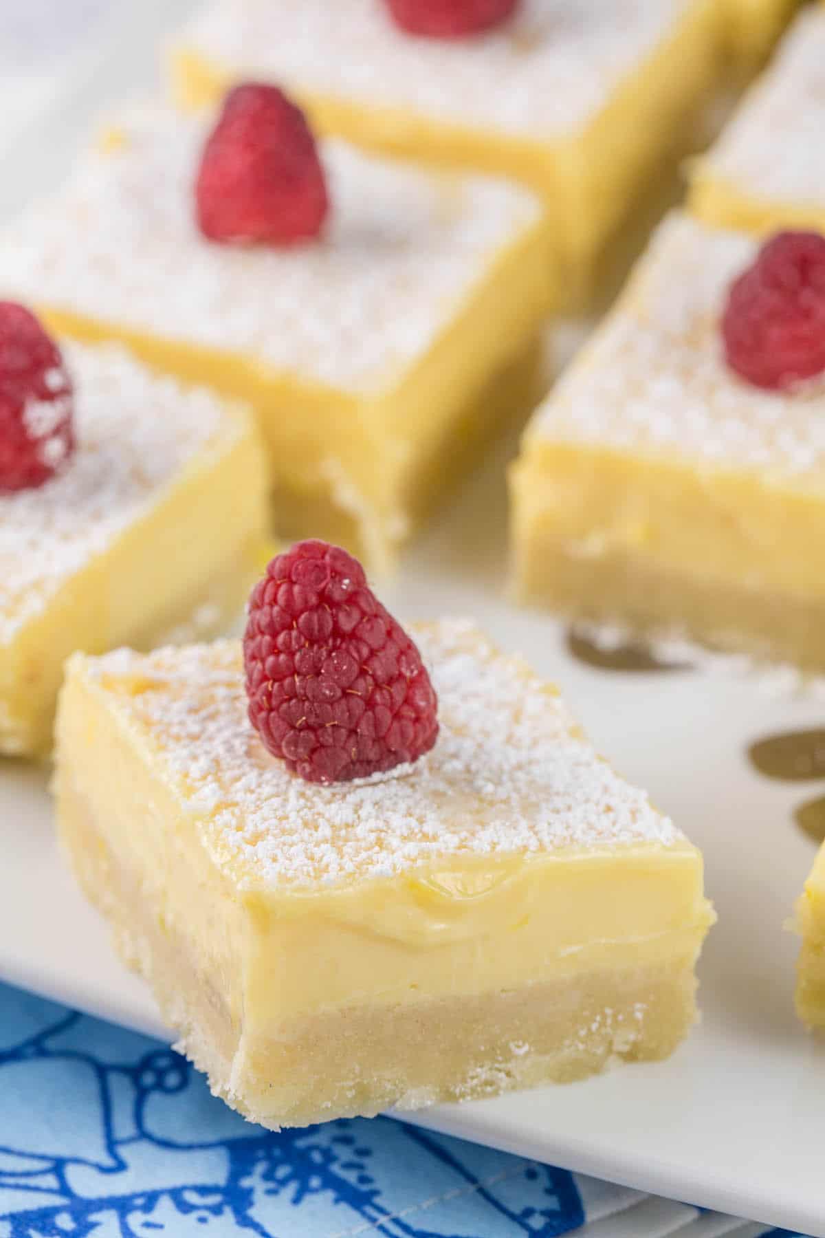 a plate of lemon pie bars decorated with powdered sugar and raspberries