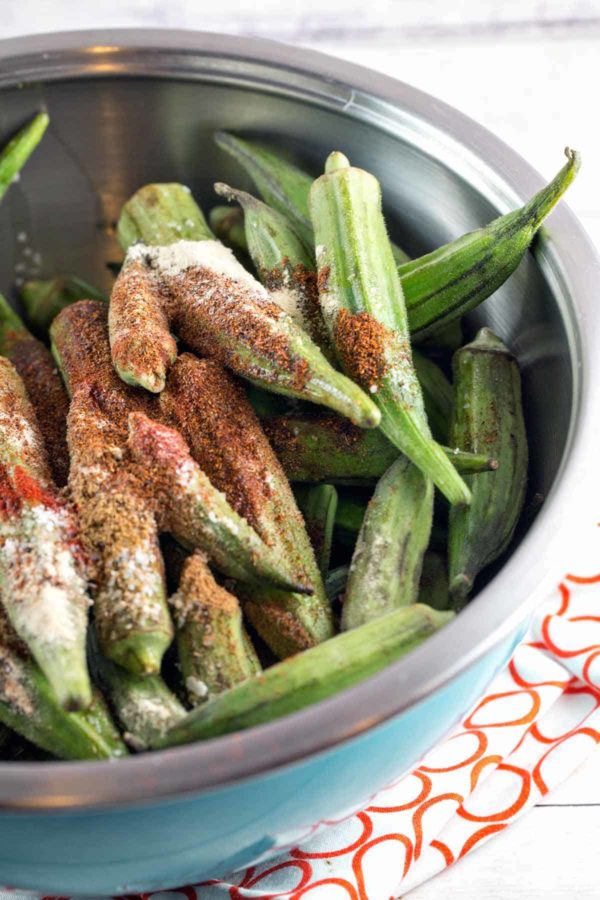 fresh bright green okra covered in spices and piled in a blue mixing bowl