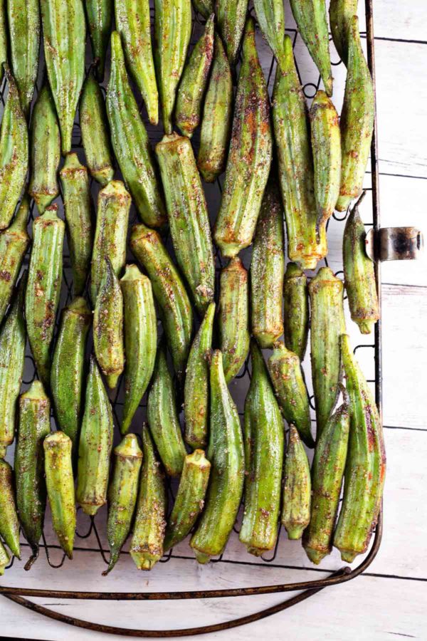 dozens of okra pods covered in spices lined up on a grill basket