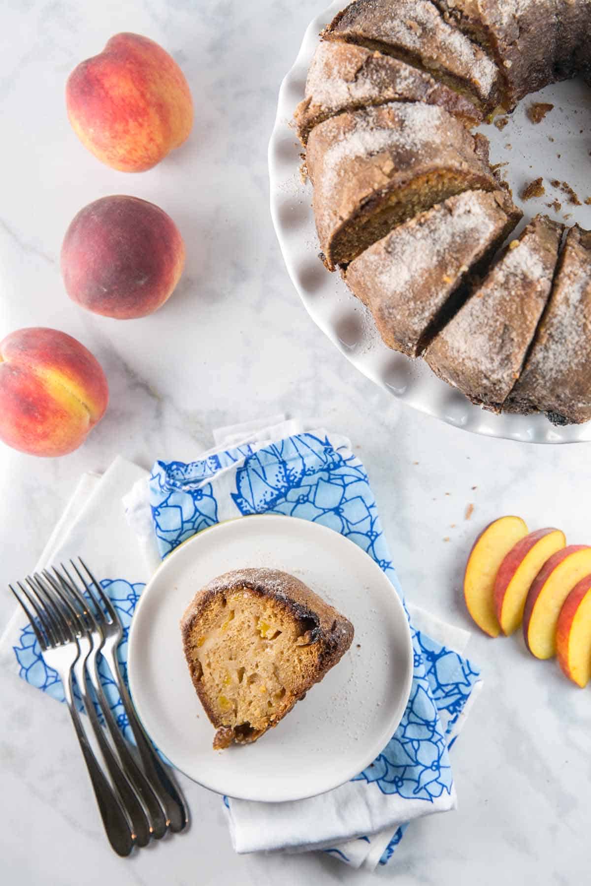 bundt cake cut into slices with one slice on a plate next to whole and sliced peaches