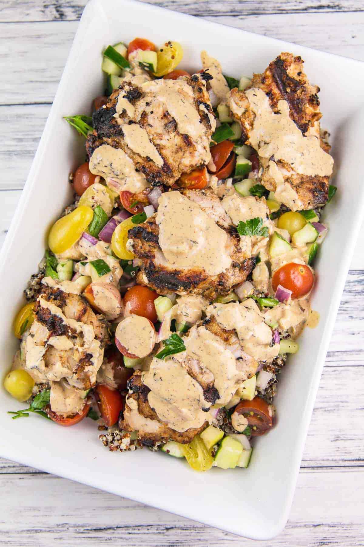 white serving dish filled with tomato cucumber salad, grilled chicken, and a creamy tahini sauce