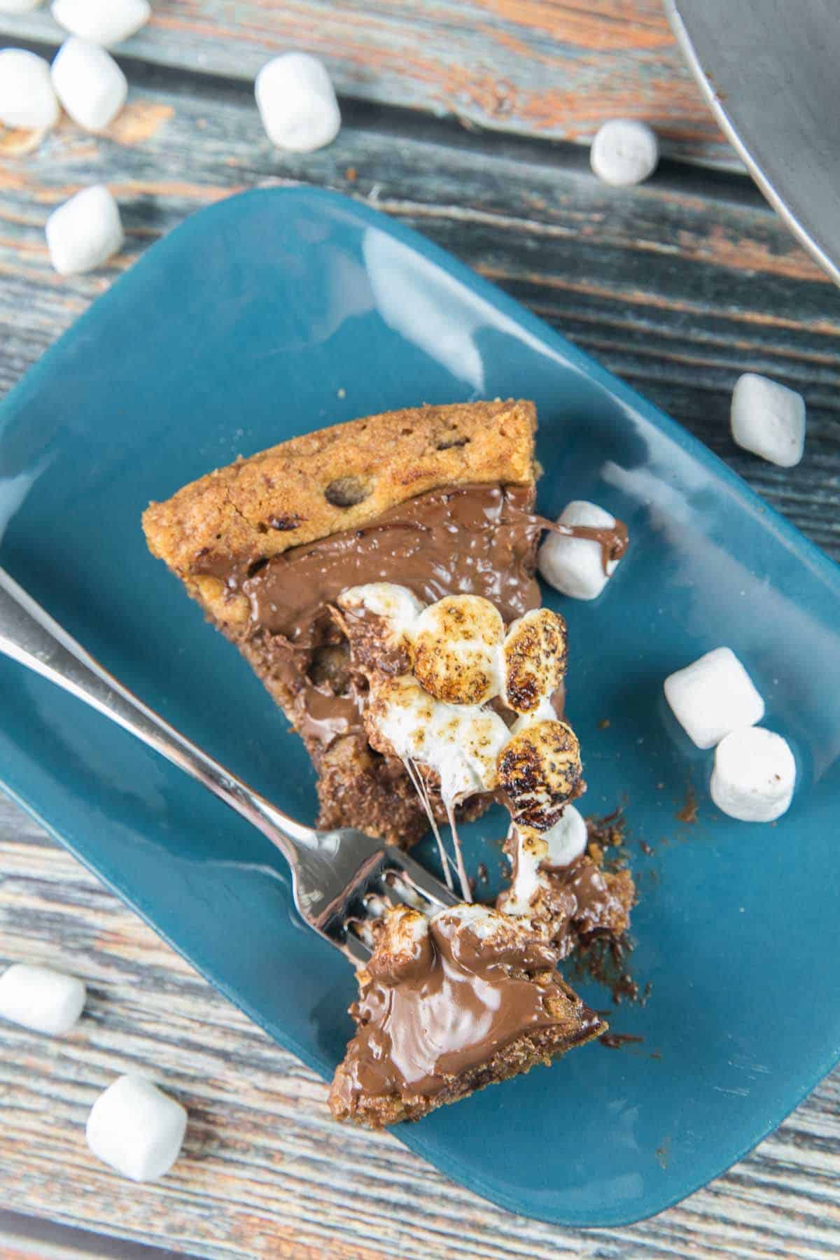 a slice of s'mores cookie cake on a plate with a fork removing one bite