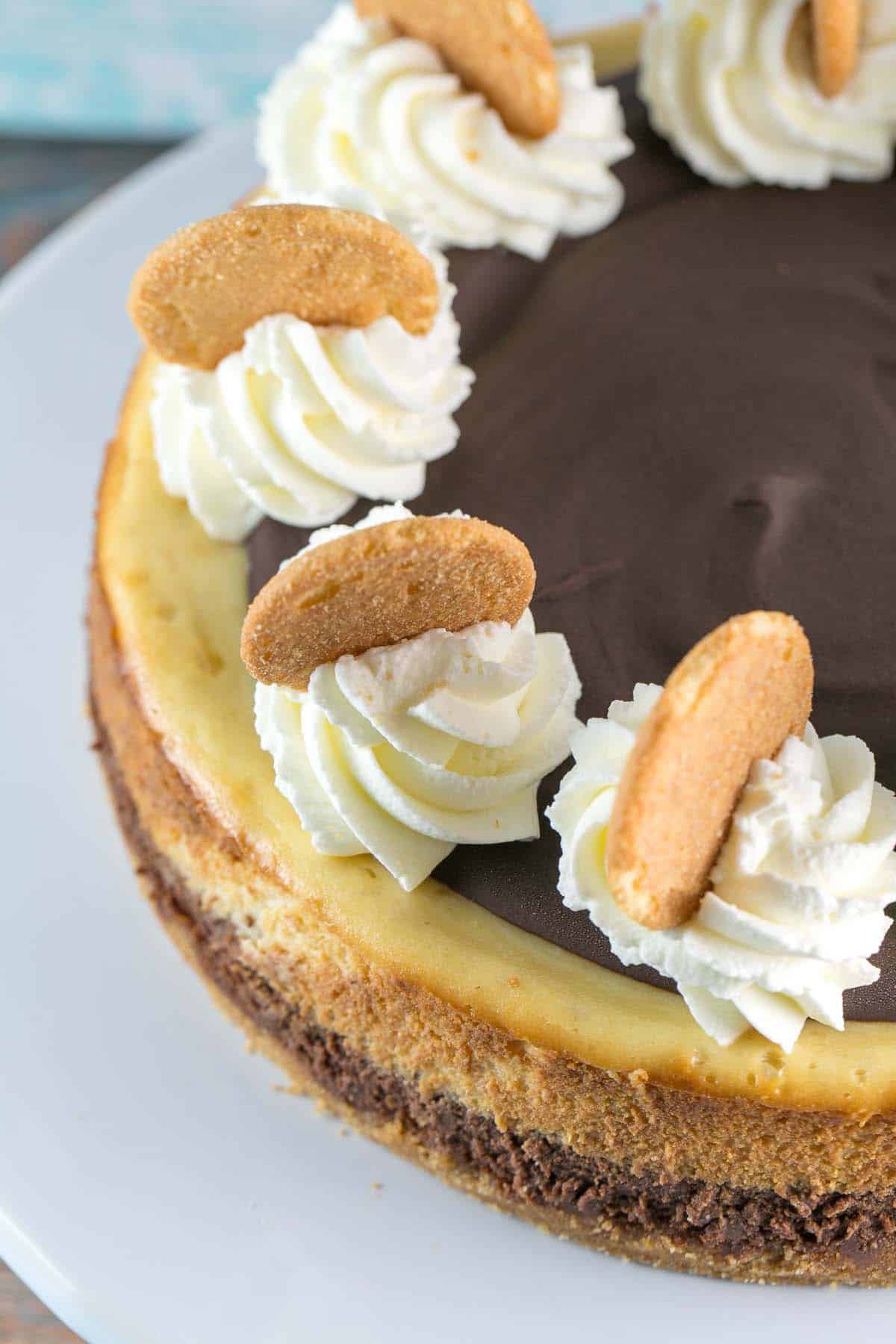 close up view of a chocolate banana cheesecake showing the swirls of whipped cream on top