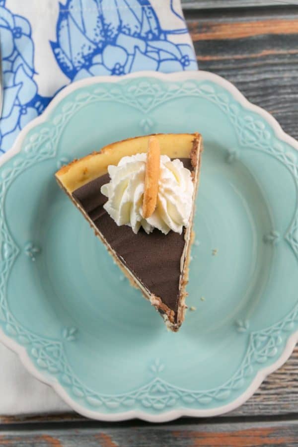 one slice of chocolate banana cheesecake with ganache topping on a blue dessert plate