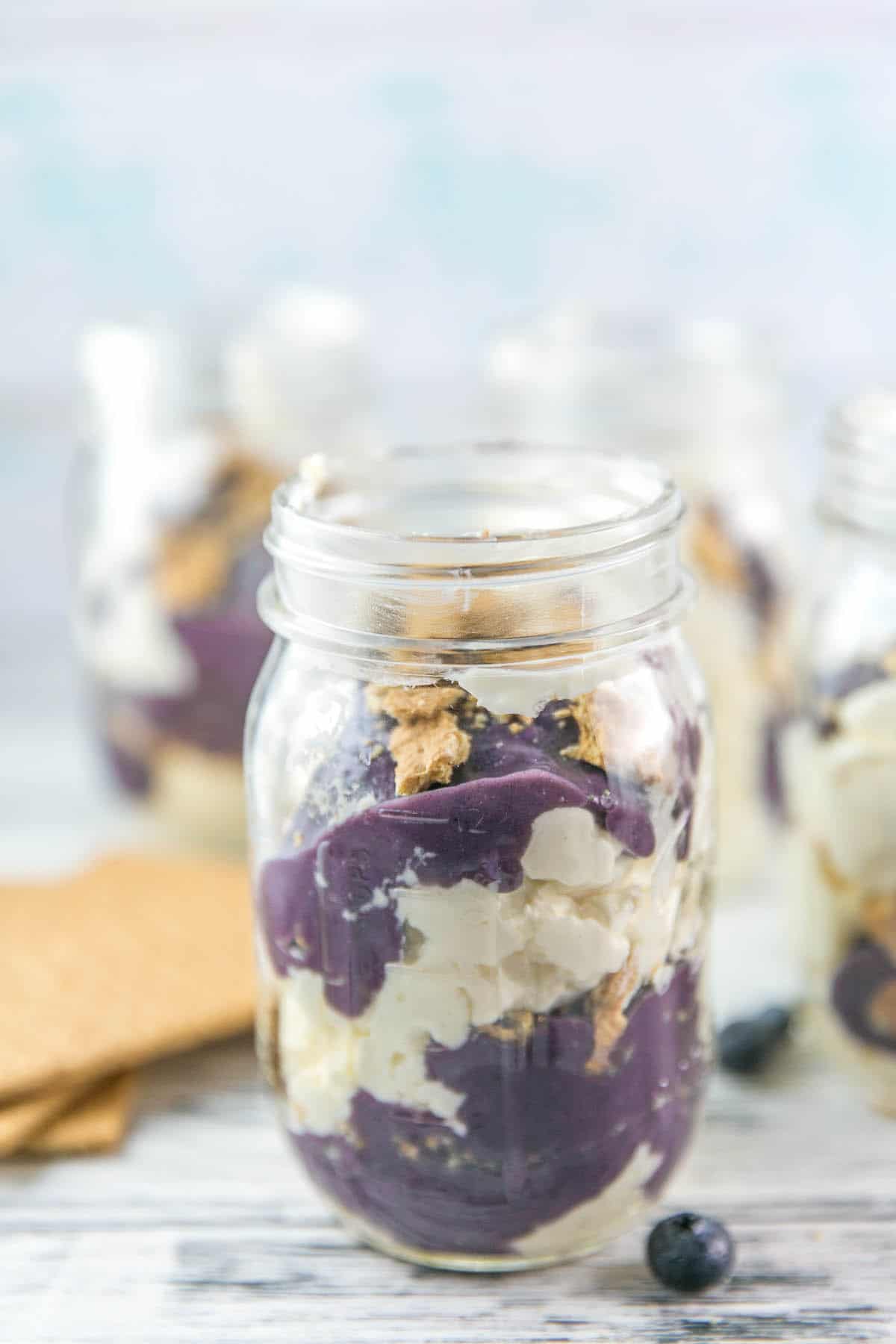 glass jar layered with cheesecake, blueberry curd, and graham cracker crumbs