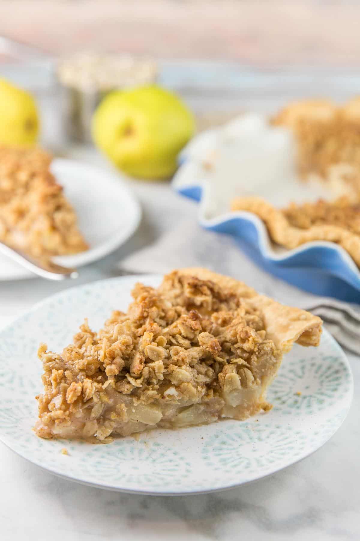 side view of a slice of caramel pear pie with a second slice and pears in the background.