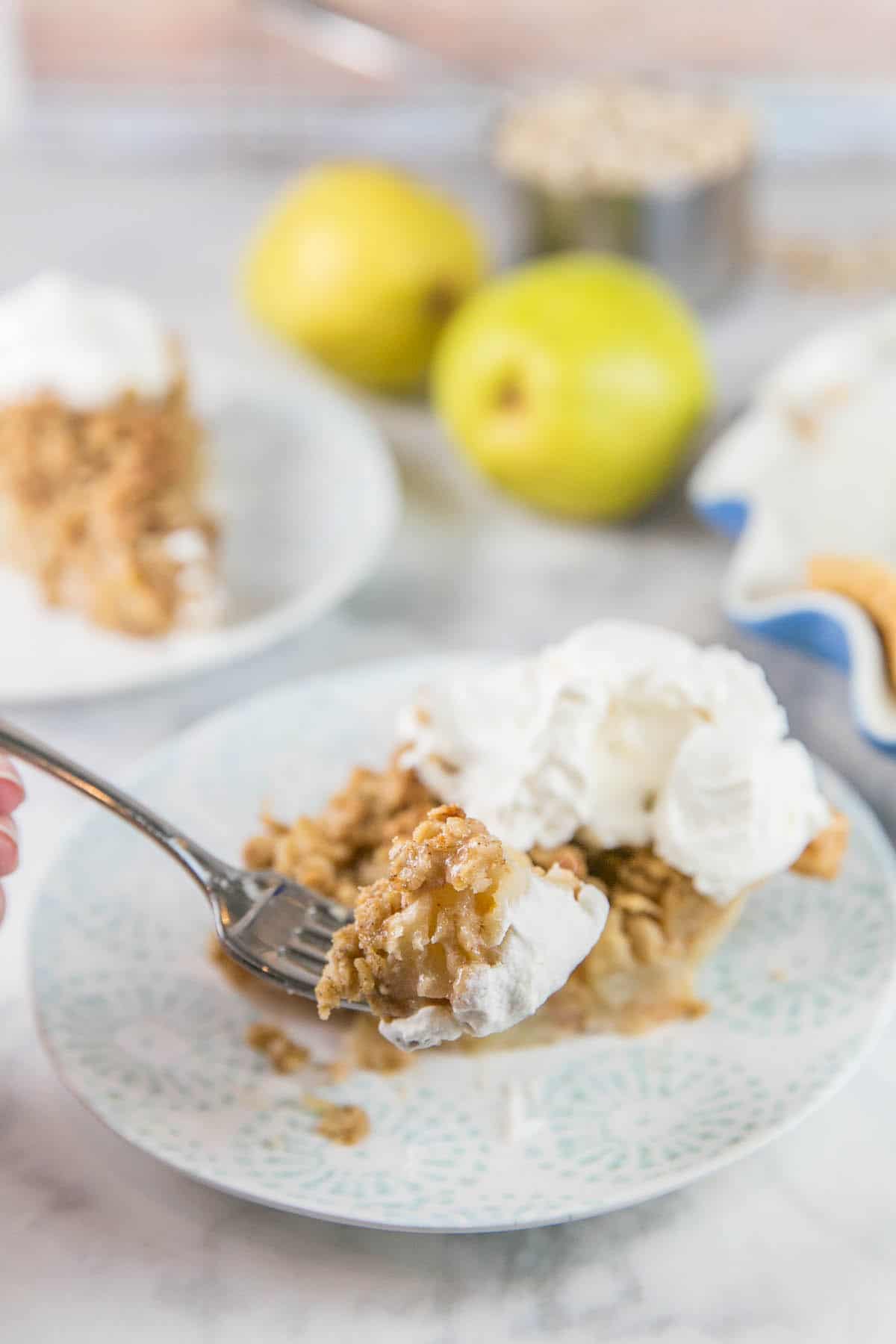 hand holding a fork with a bite of caramel pear pie on the fork and pie visible in the background.