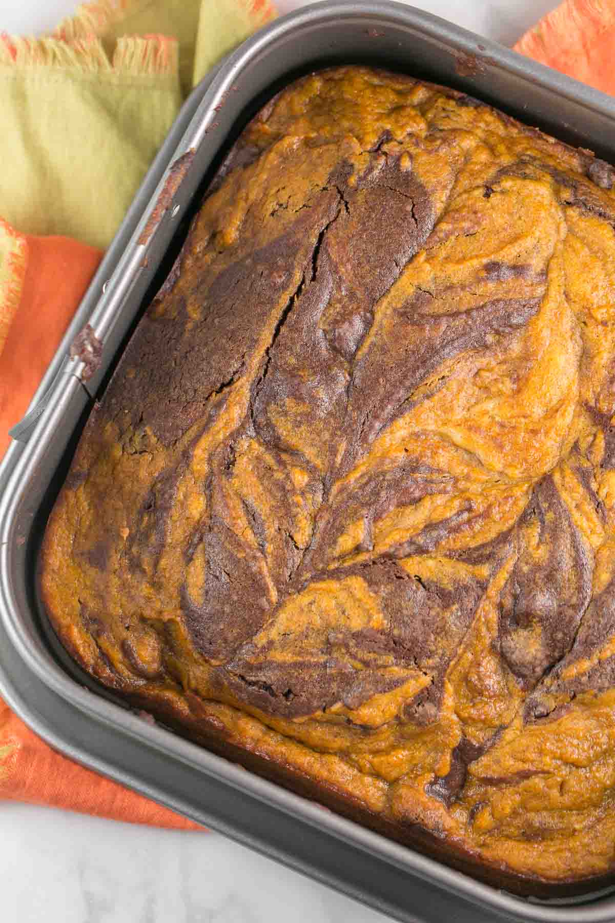 square pan of pumpkin swirl brownies on an orange and yellow dishtowel.