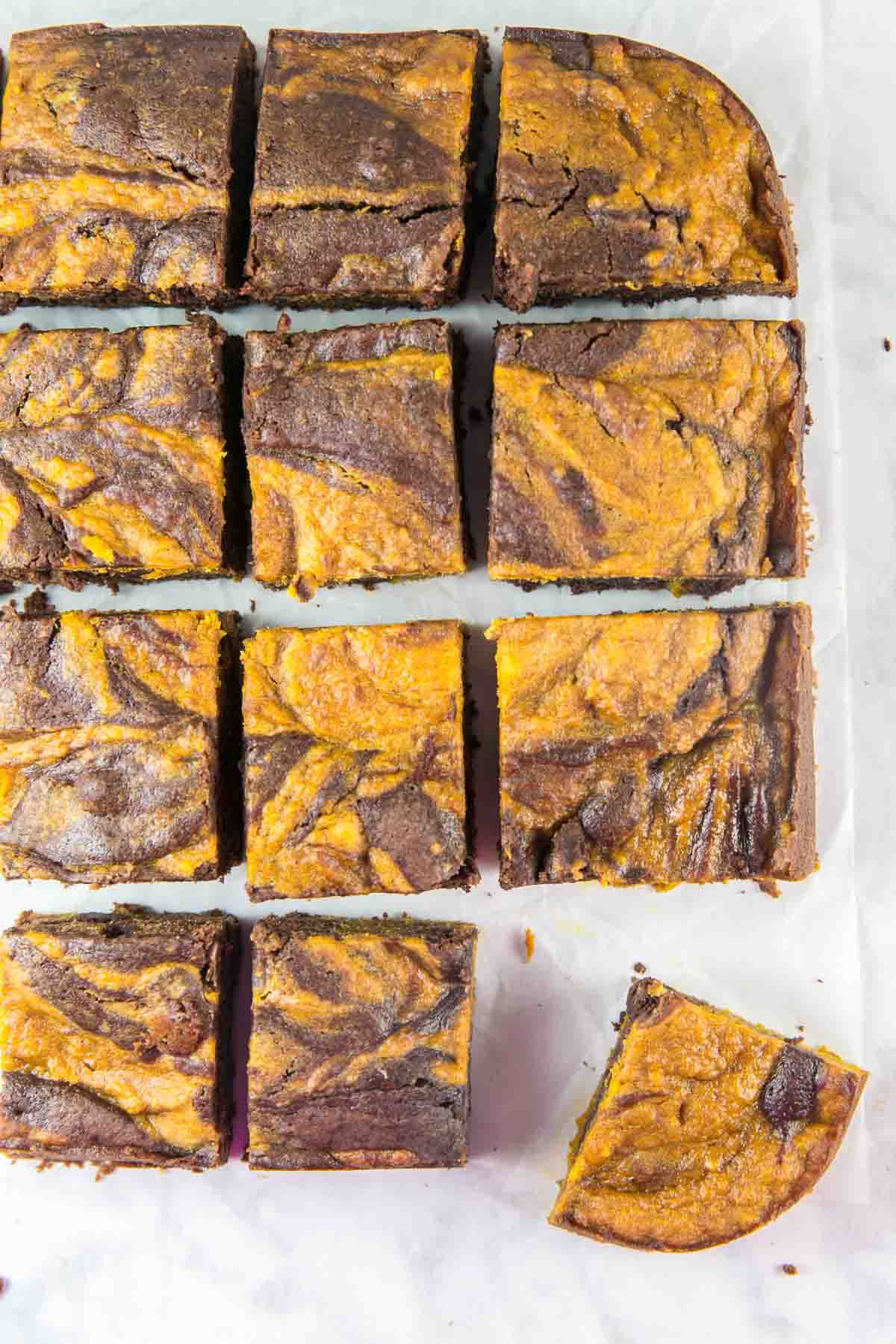 pumpkin swirl brownies on a white background lined up in a square with one corner brownie pulled out