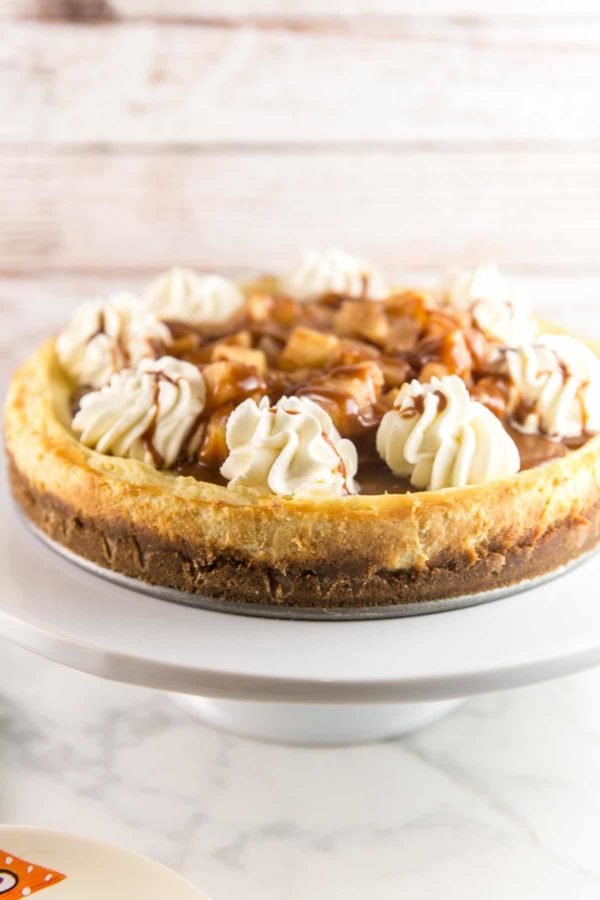 side view of a cheesecake covered with whipped cream, cooked apples, and salted caramel.