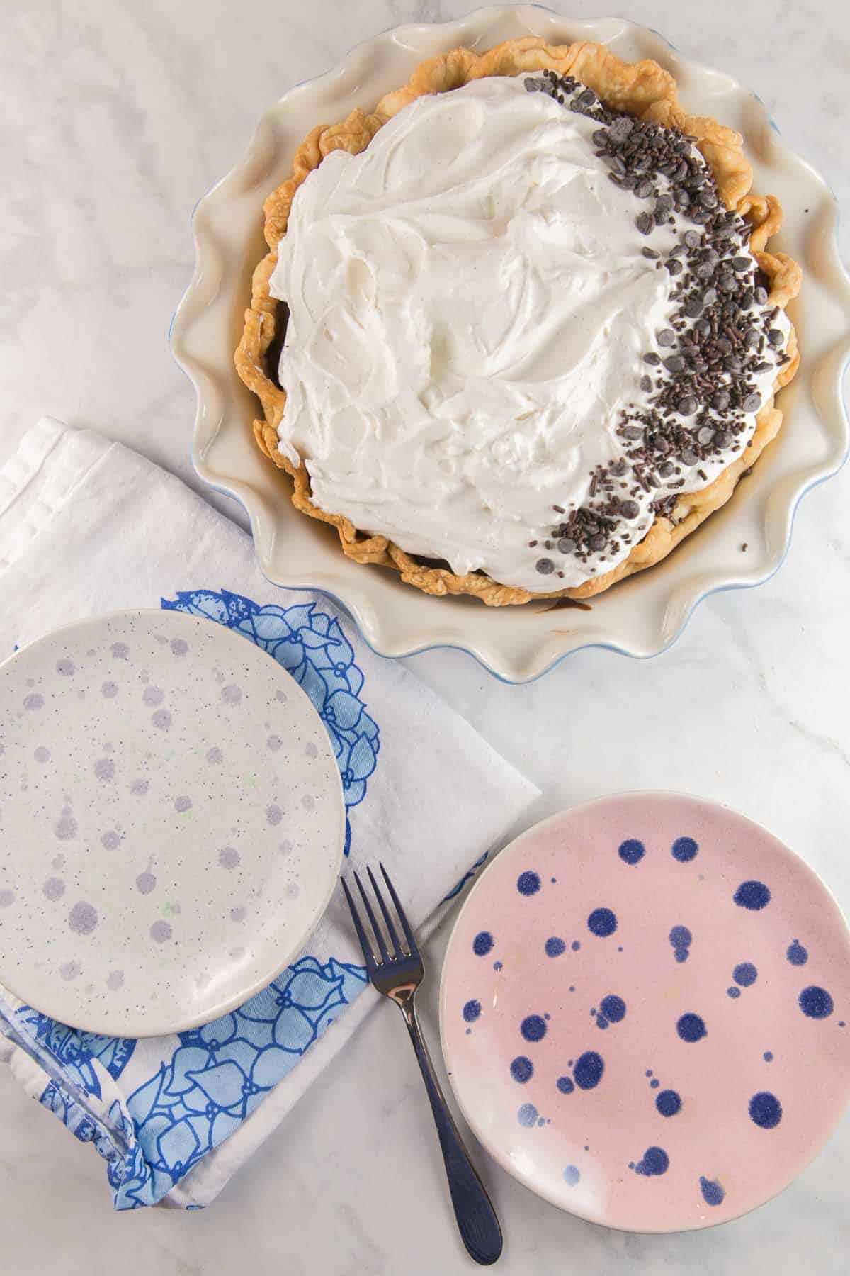 pie dish full of chocolate cream pie next two two colorful dessert plates