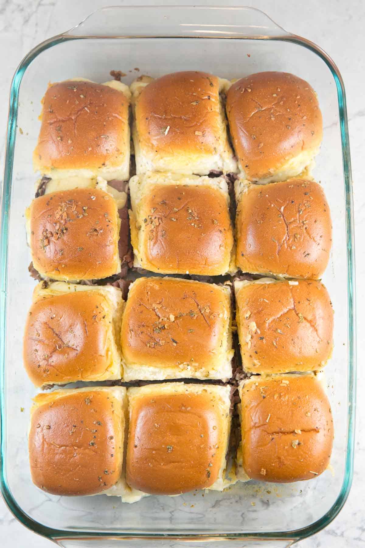 overhead image of 12 baked roast beef sliders in a glass baking dish cut apart and ready to serve