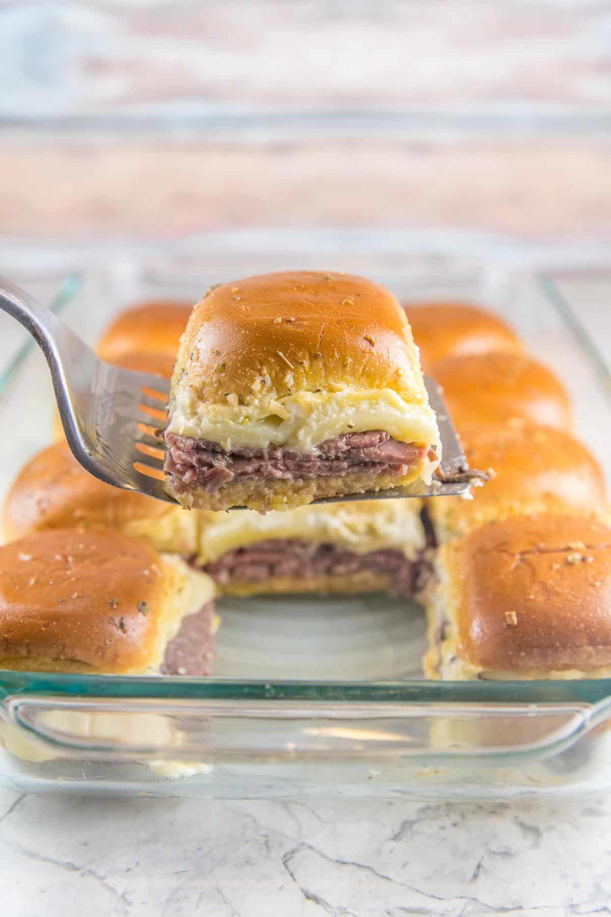 one hot baked roast beef slider sandwich being lifted out of the pan on a metal spatula