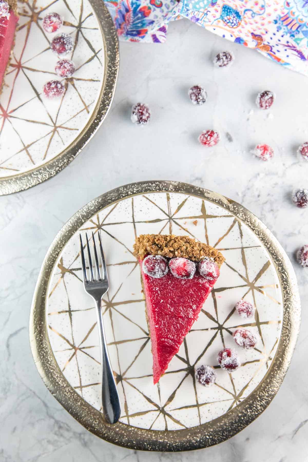 one slice of cranberry curd pie with a gingersnap hazel crust plated with sugared cranberries and a dessert fork.