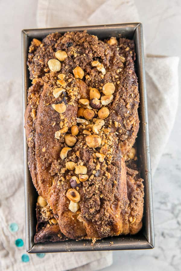 baked loaf of cinnamon hazelnut babka in a loaf pan with chopped hazelnuts scattered on top.