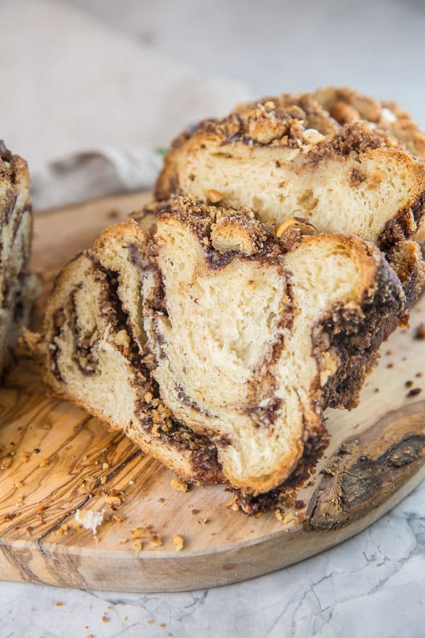 a loaf of cinnamon hazelnut babka sliced on a wooden cutting board.