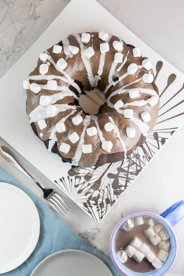 chocolate bundt cake on a silver snowflake serving plate with mugs of hot chocolate nearby.