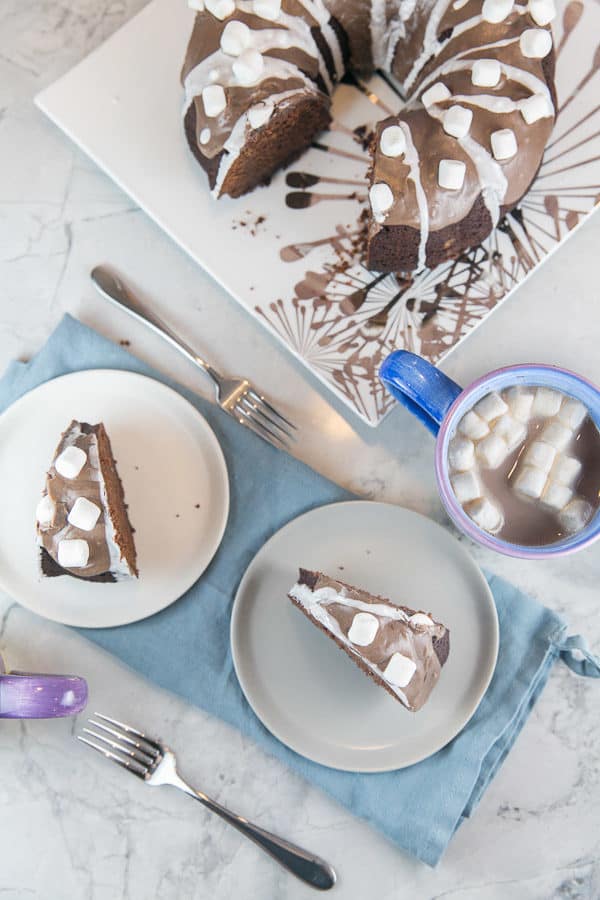 two slices of hot chocolate bundt cake covered with miniature marshmallows on white and grey dessert plates