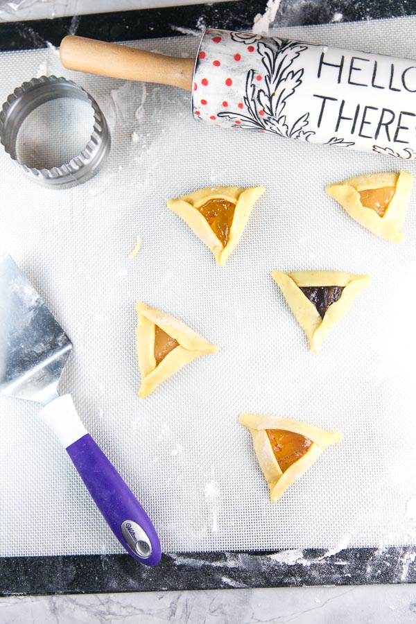 folded unbaked hamantaschen next to a decorative rolling pin and biscuit cutter
