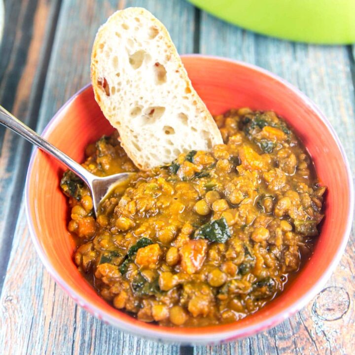 bowl of kale and lentil soup with a piece of bread resting on the side