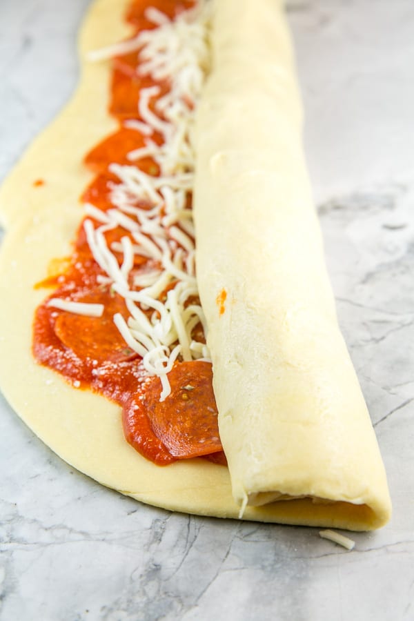 babka dough covered with pizza toppings halfway rolled into a log.