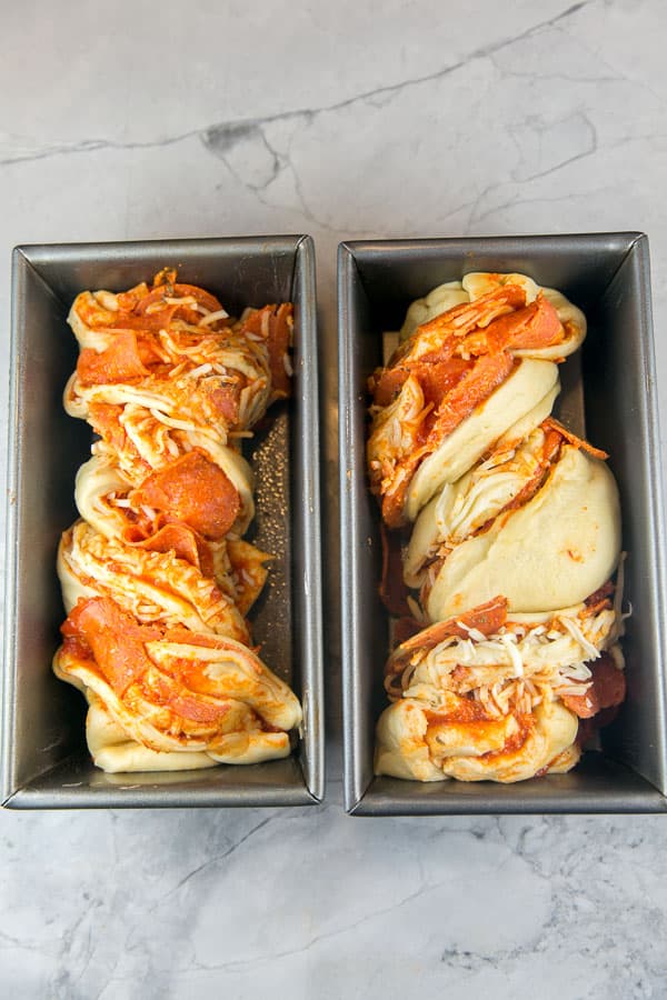 two unbaked loaves of pizza babka with tomato sauce and pepperoni spilling out the sides.