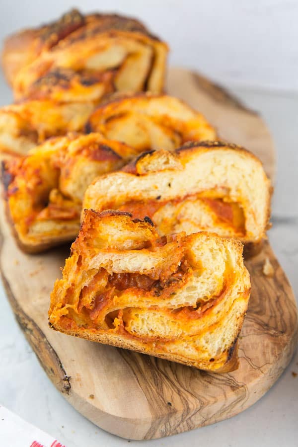 a sliced pizza babka on a wooden cutting board with swirled slices containing tomato sauce and pepperoni
