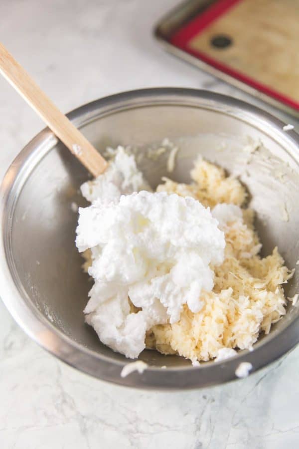 a mixing bowl full of coconut mixture topped with a pile of fluffy whipped egg whites