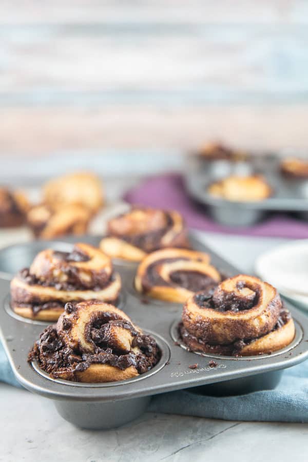 side view of babka muffins with chocolate swirls towering over the edge of a muffin tin
