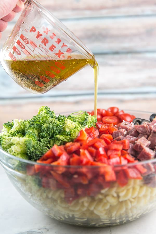 italian pasta salad in a glass bowl with homemade dressing being poured over the top