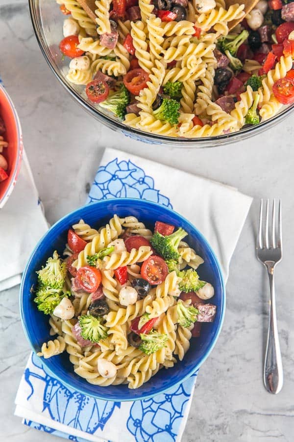 a blue bowl filled with italian pasta salad sitting on a blue floral napkin