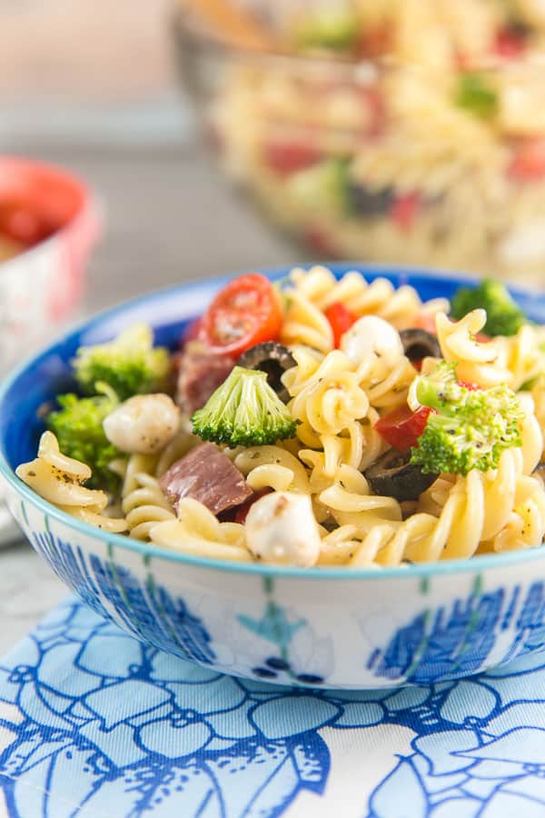 side view of a blue and white bowl filled with a heaping pile of colorful italian pasta salad