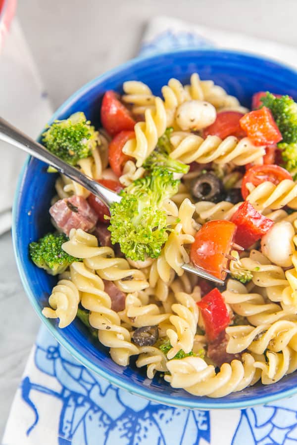 overhead view of a bowl of italian pasta salad with rotini, broccoli, red peppers, olives, and salami visible