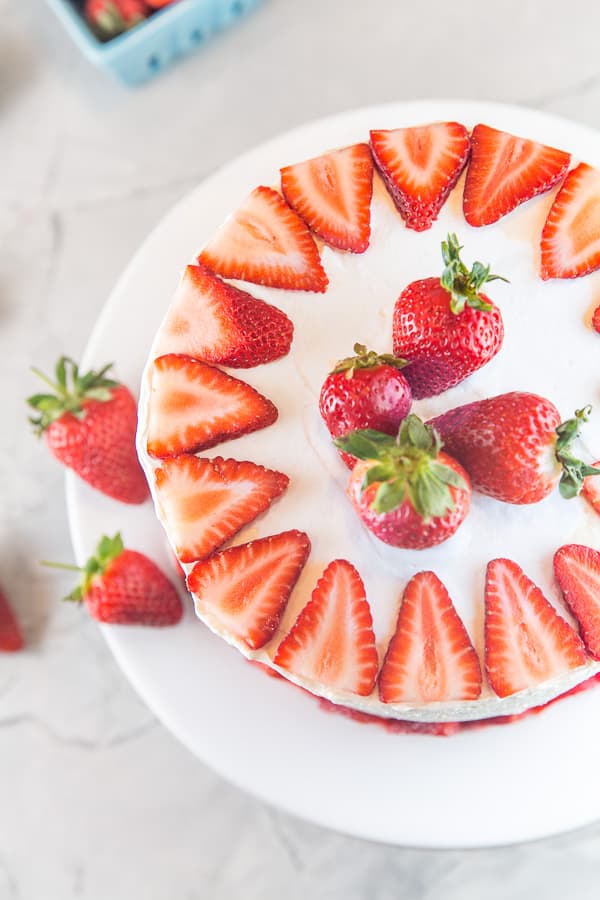 overhead view of a strawberry layer cake decorated with sliced strawberries along the edges and whole strawberries in the center