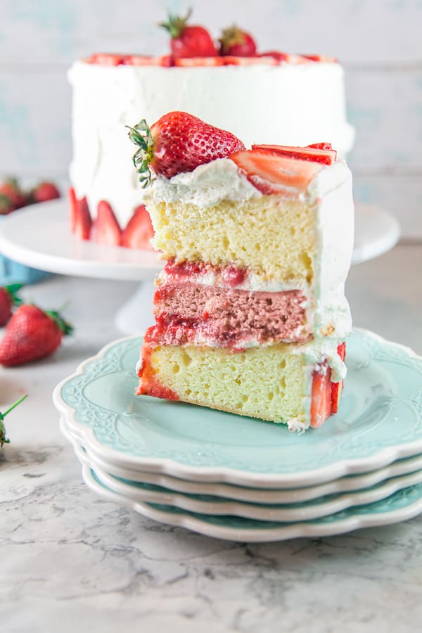 a cut slice of a three layer strawberry layer cake on blue dessert plates with vanilla and strawberry layers of cake