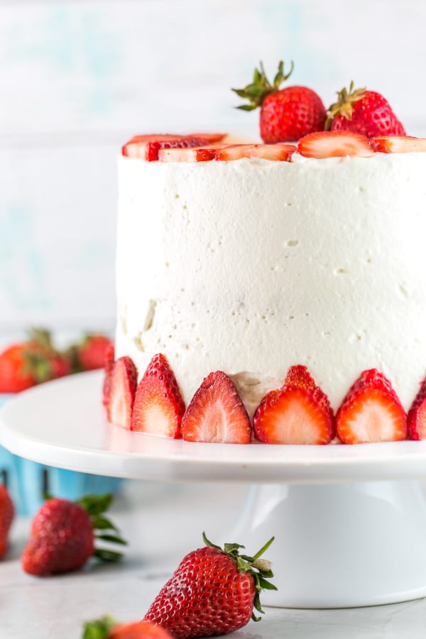 a three layer strawberry cake decorated with sliced strawberries on a white cake stand