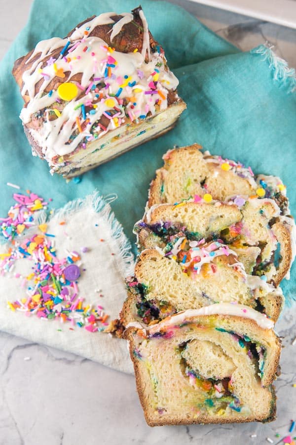 three slices of funfetti babka next to the uncut babka loaf surrounded by sprinkles