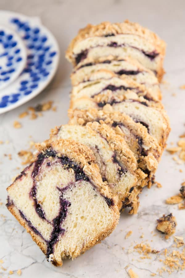slices of blueberry babka lined up on a marble counter surrounded by crumbs of almond streusel topping