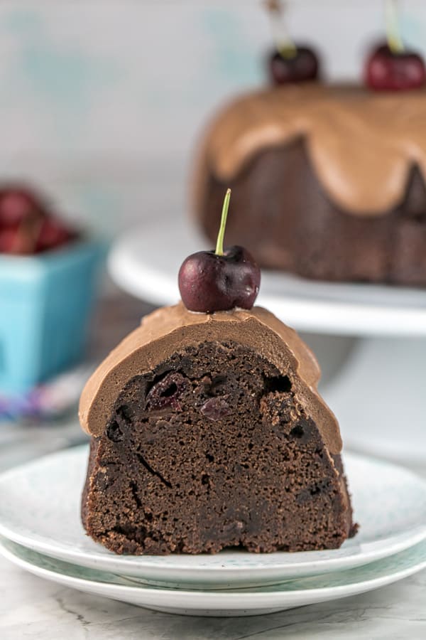 one slice of chocolate cherry bundt cake on stack of dessert plates showing the dark chocolate interior and thick layer of fudge frosting