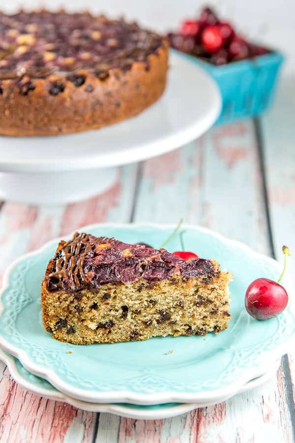 side view of a slice of chocolate chip cherry upside down cake on a blue dessert plate showing the chocolate chip studded fluffy thick slice of cake with a layer of fresh cherries on top