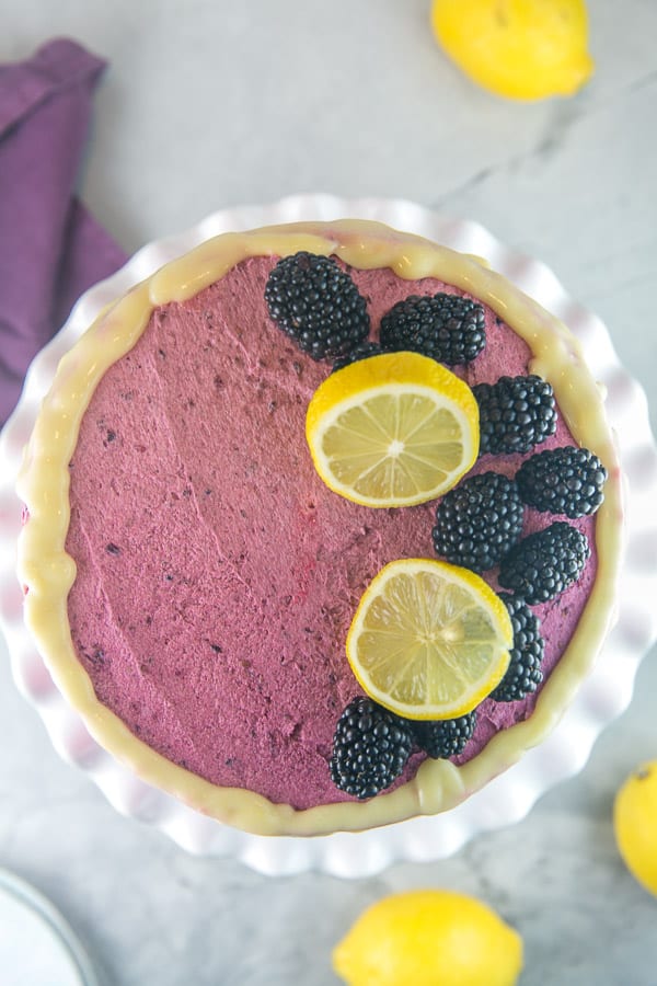 overhead view of a lemon curd layer cake decorated with blackberry frosting, lemon glaze, slices of lemon, and whole blackberries