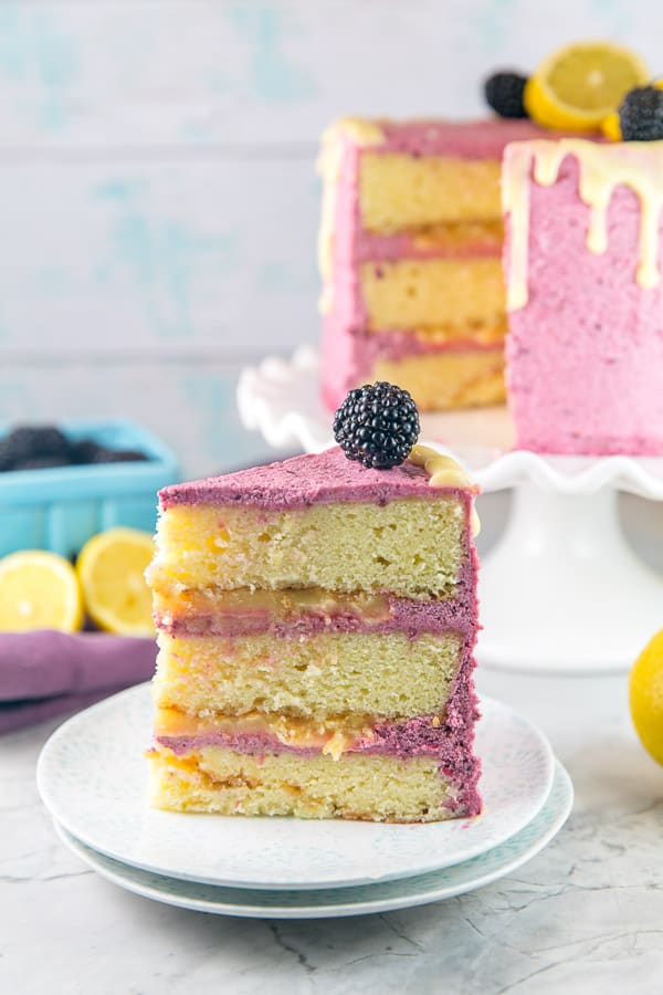 a slice of lemon curd cake showing three layers of cake, lemon curd filling, and blackberry buttercream frosting