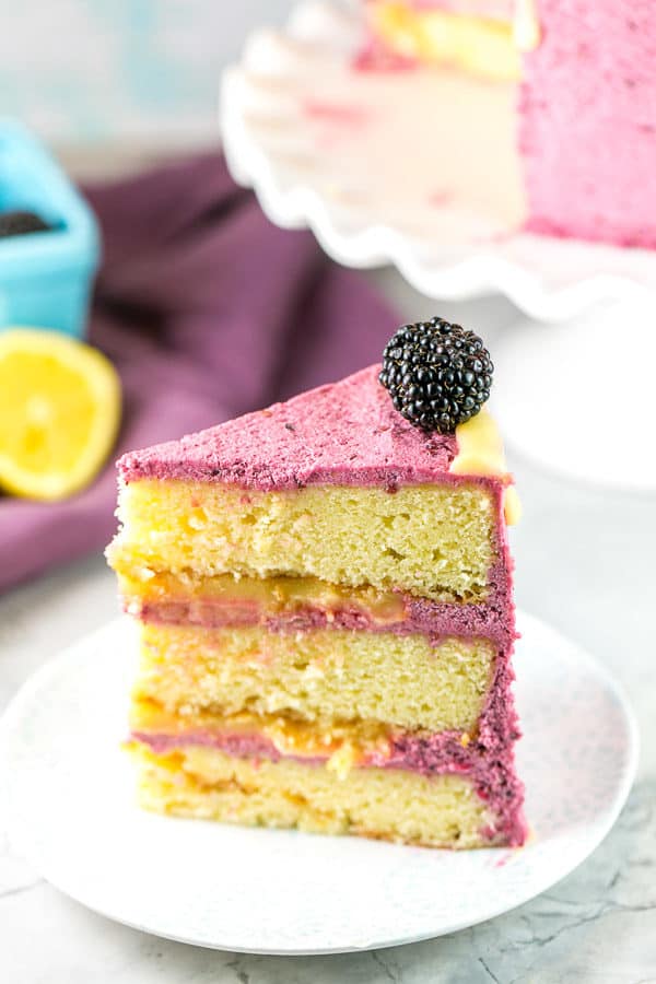 a slice of lemon curd cake with blackberry buttercream frosting on a white dessert plate